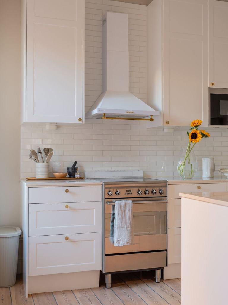 A white shaker kitchen with gold hardware and a white subway tile backsplash