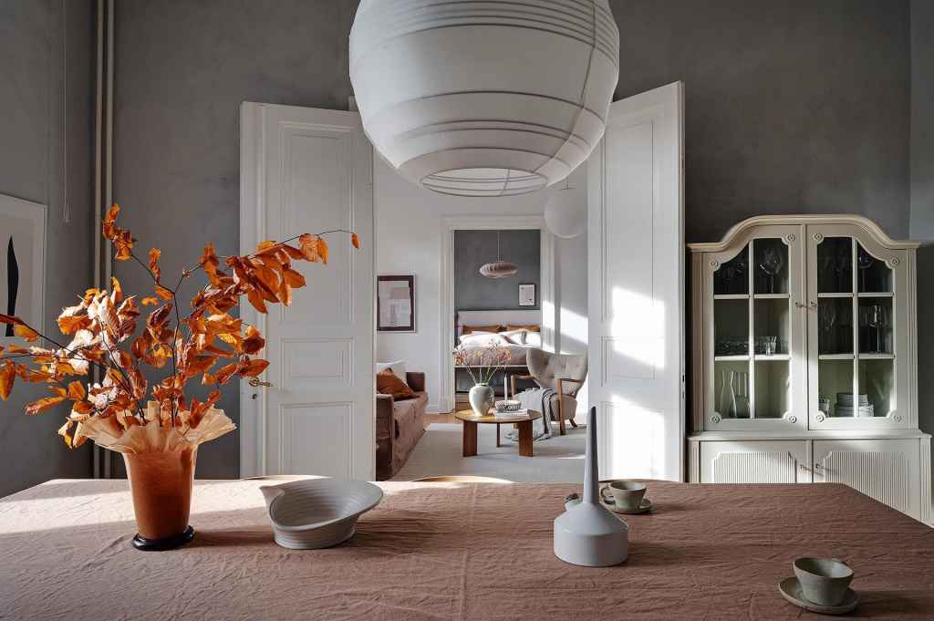 A dining room with grey limewash walls and a warm palette in the accessories and furniture