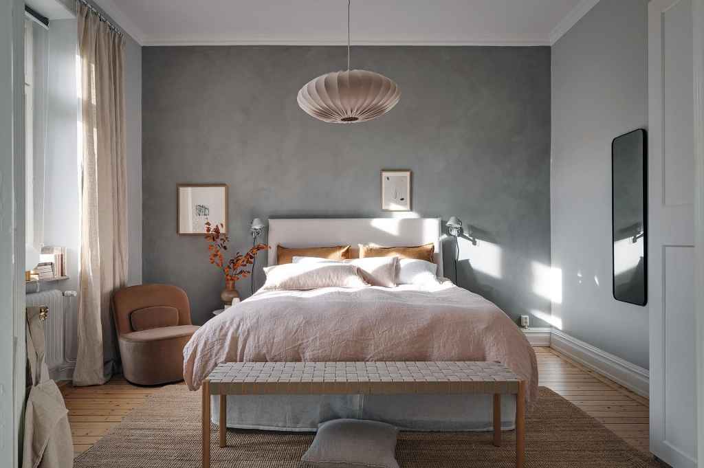 A bedroom with a grey limewash accent wall and a beige color palette in the textiles and accessories