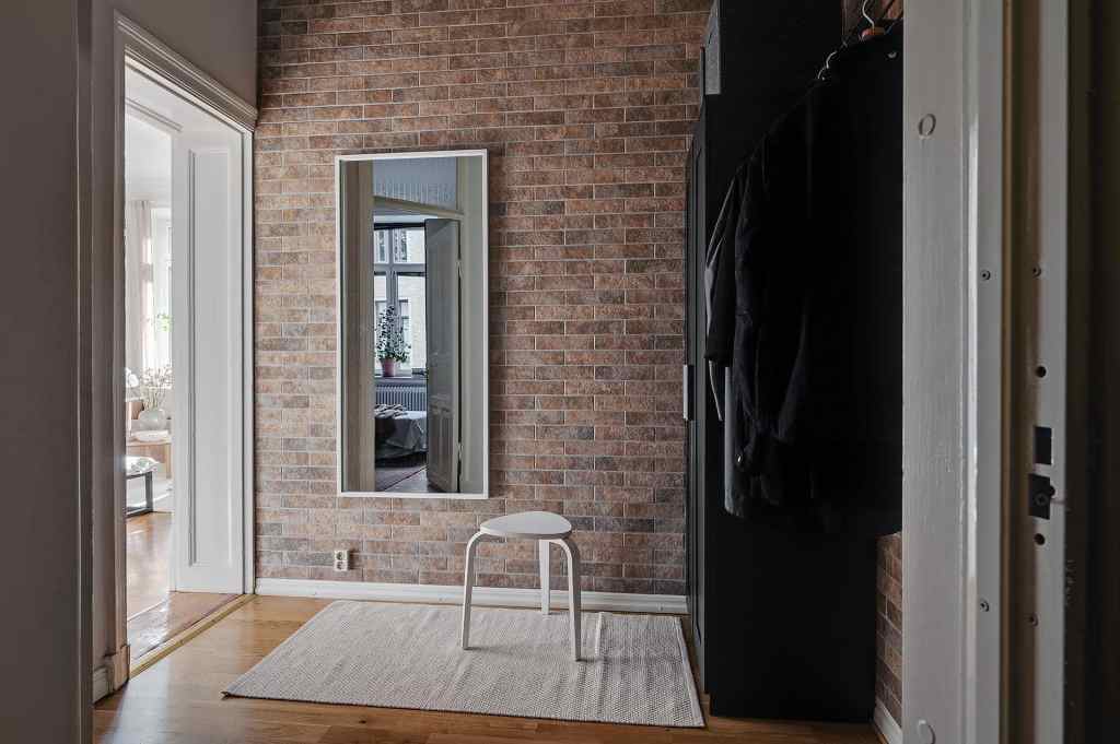 A small entryway with a fake brick wall and a black wardrobe