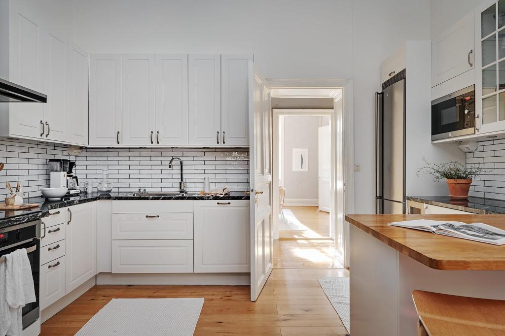 A simple white kitchen with black marble countertops and dark metal hardware