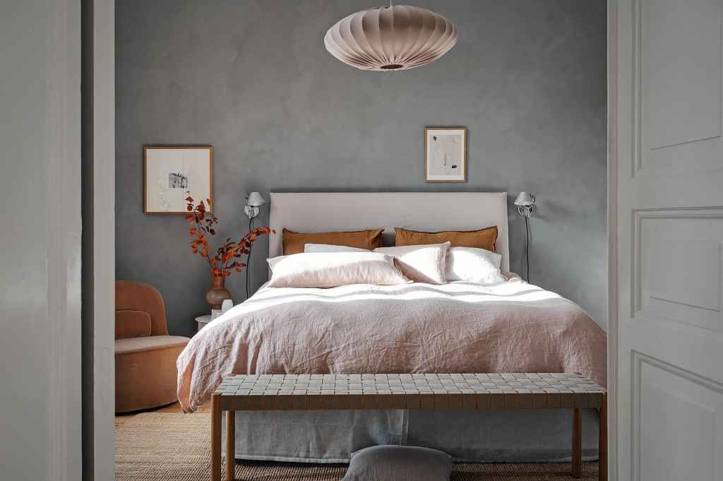 A bedroom with a grey limewash accent wall and a beige color palette in the textiles and accessories