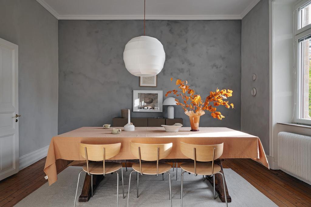 A dining room with grey limewash walls and a warm palette in the accessories and furniture