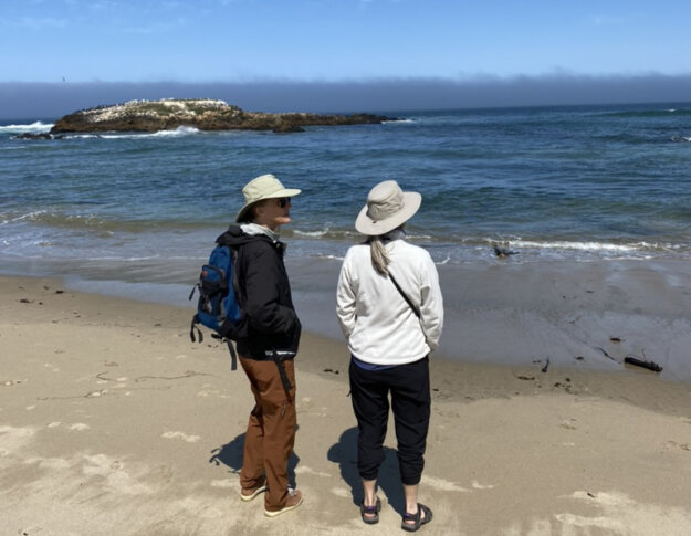 Two women in hiking gear at Pescadero in California, looking out at the Pacific