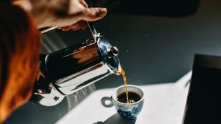 Woman's hand pouring moka pot coffee into cup