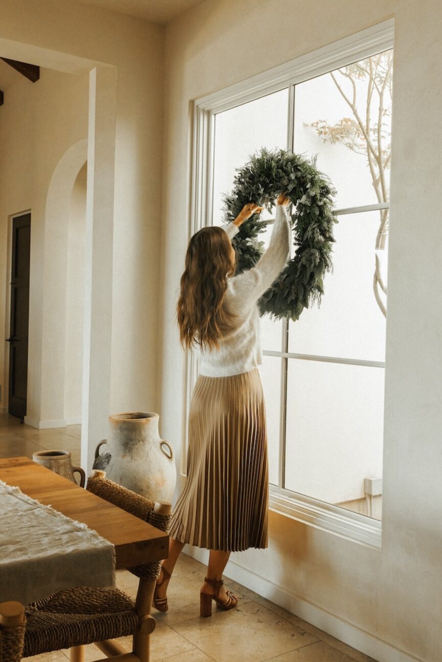 Camille Styles wearing holiday outfit formula hanging up wreath