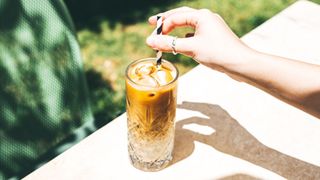 Ice coffee sitting in tall glass with long paper straw