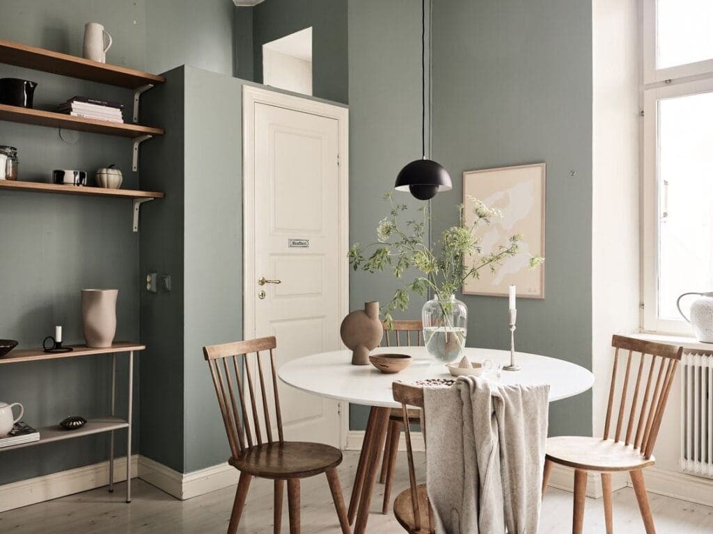 An eat-in kitchen with soft sage green walls and an ivory pantry door