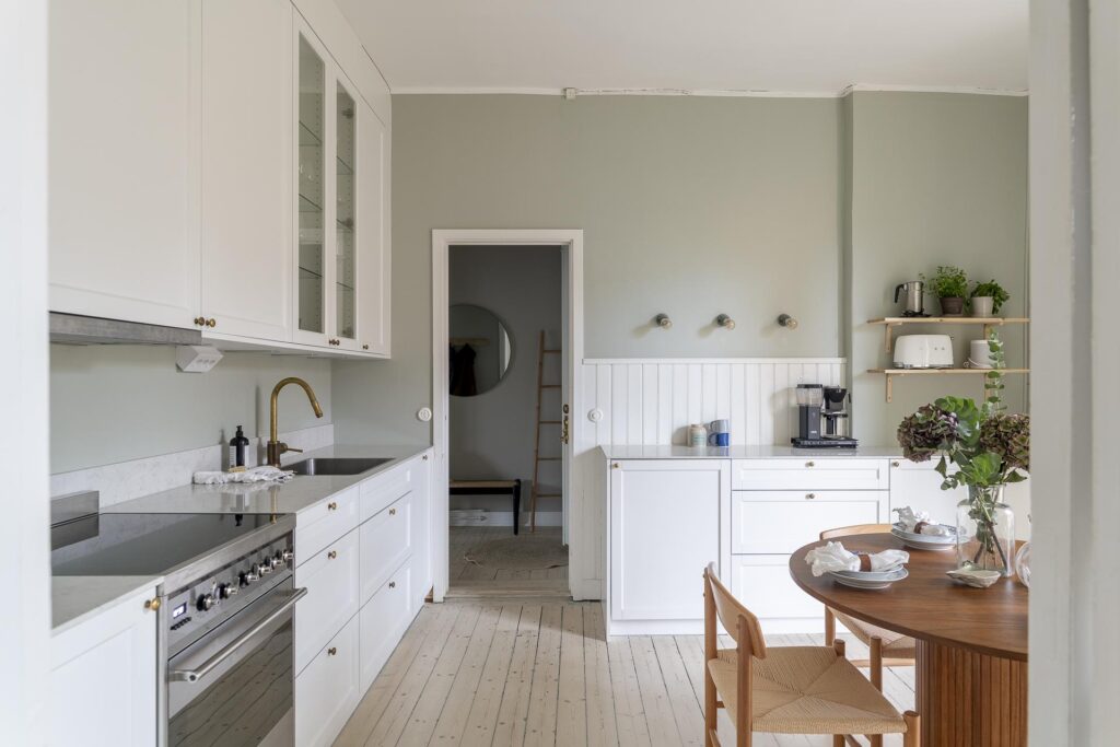 A light sage green kitchen wall color enhancing a minimal white shaker kitchen