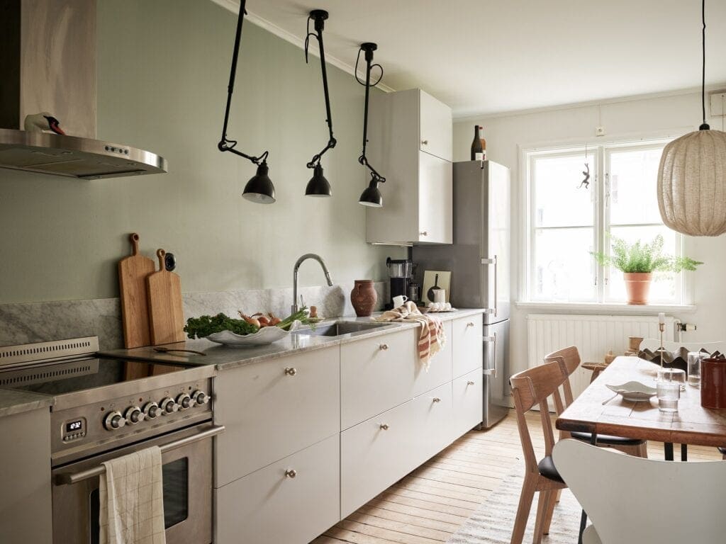 A sage green feature wall enhancing a white kitchen with black industrial lighting