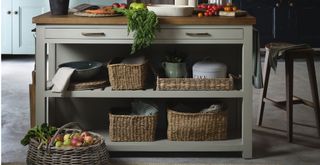 Close up of a green painted wooden kitchen island with seagrass storage baskets to show how to make a kitchen cosy