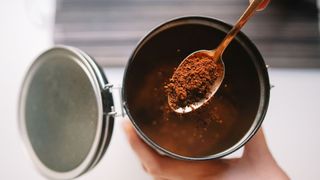 Ground coffee scattering into tin from metal spoon