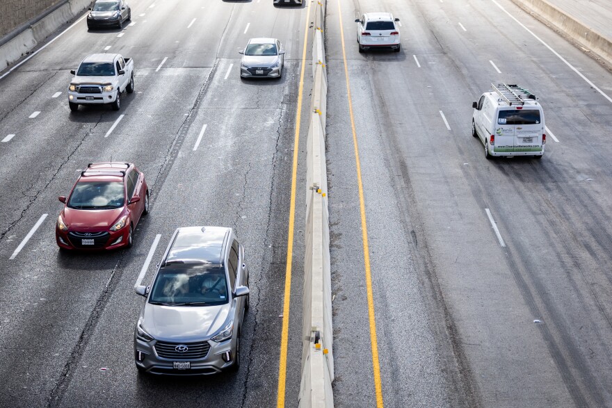 Traffic passes beneath the Tech Ridge Boulevard bridge over I-35. A handful of vehicles appear motionless on the black asphalt of the highway. 