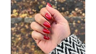 A close up of Digital Beauty Editor, Aleesha Badkar's red almond nails, in front of a wintery pavement background