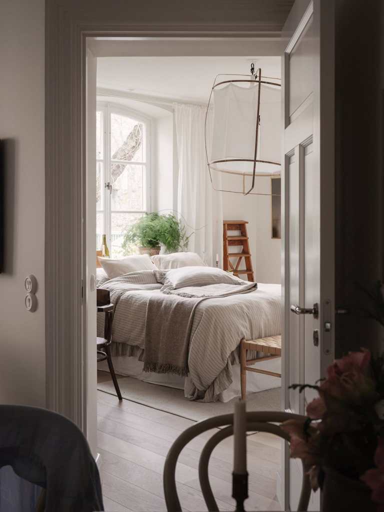 A bedroom with beige and white textiles and natural wood tones