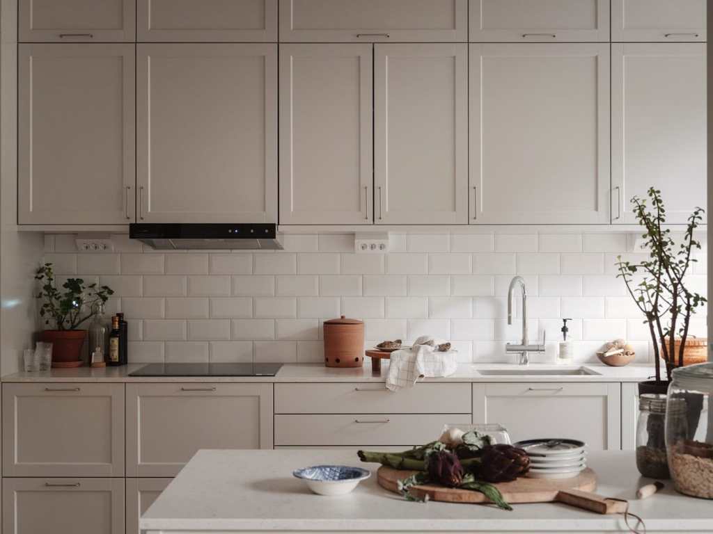 A light grey kitchen with a white subway tile backsplash, stainless steel hardware and a small kitchen island