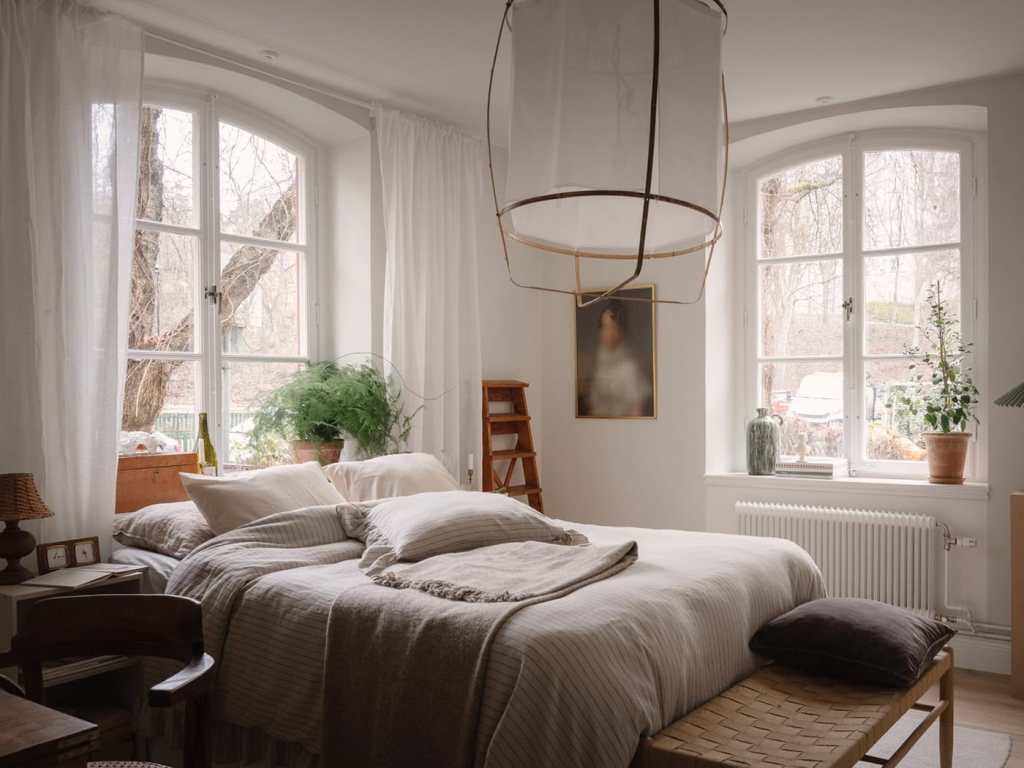 A bedroom with beige and white textiles and natural wood tones