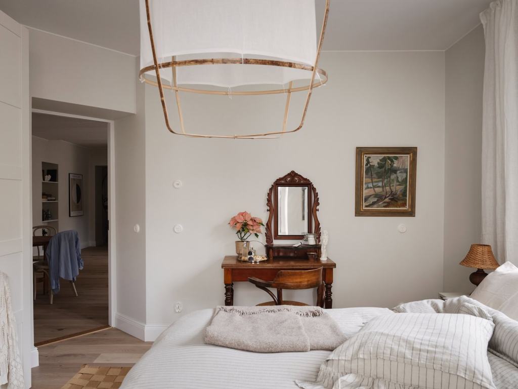 A bedroom with beige and white textiles and a vintage vanity