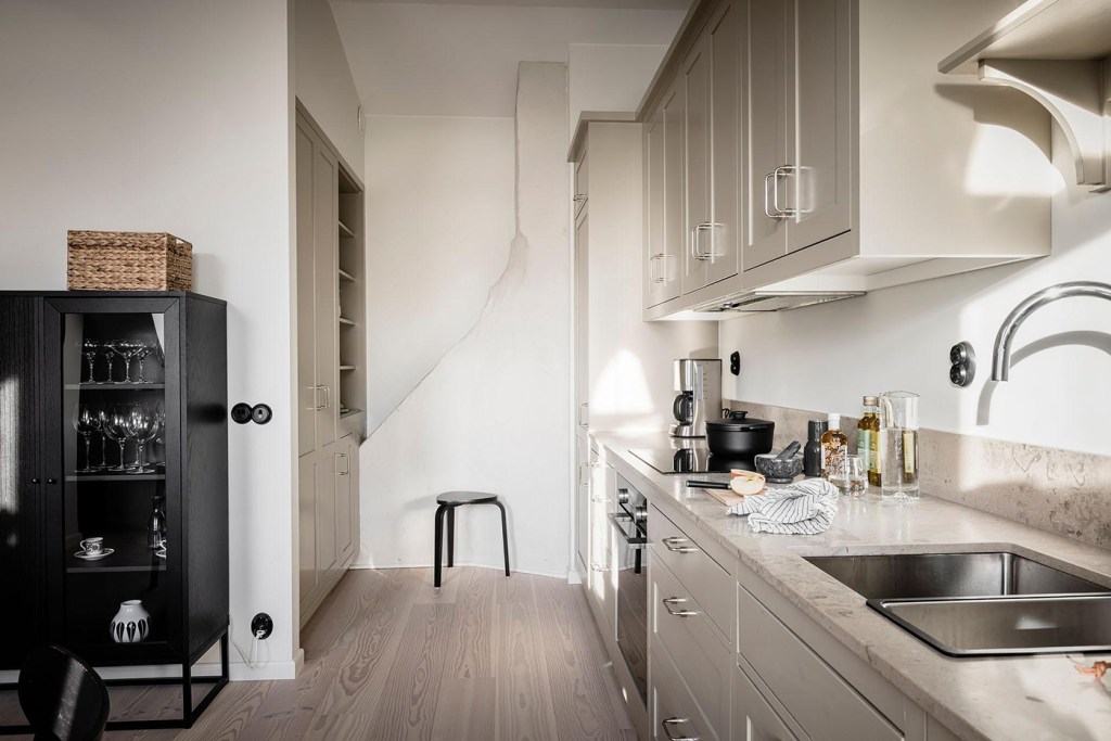 A beige shaker kitchen with a beige limestone countertop, chrome hardware and a black dining table