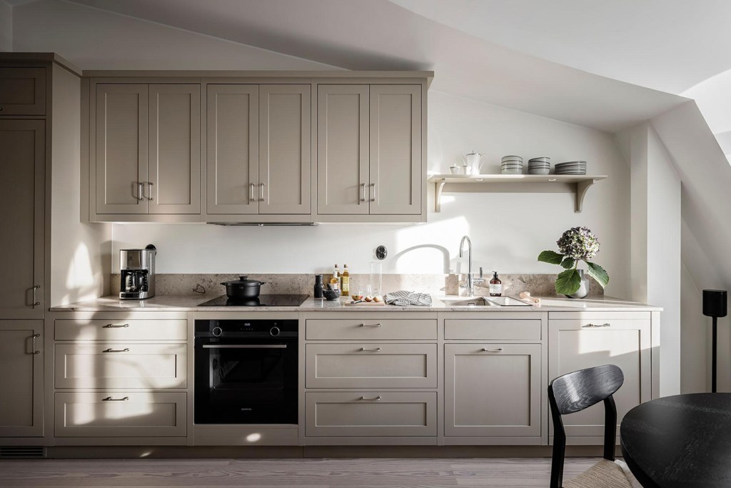 A beige shaker kitchen with a beige limestone countertop, chrome hardware and a black dining table