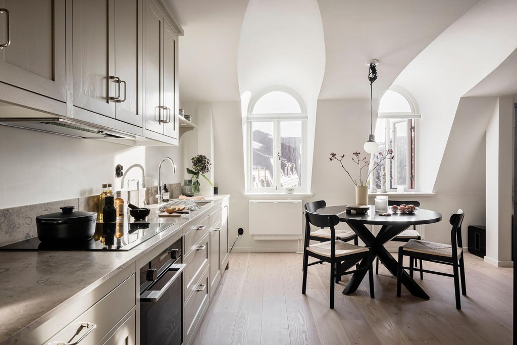 A beige shaker kitchen with a beige limestone countertop, chrome hardware and a black dining table