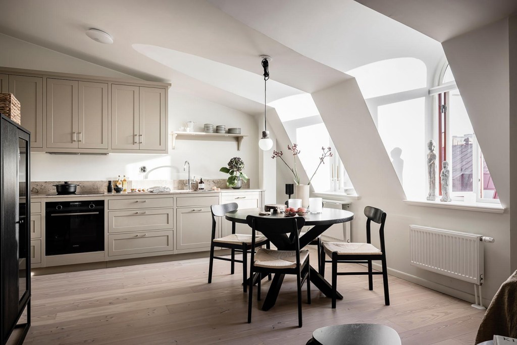 A beige shaker kitchen with a beige limestone countertop, chrome hardware and a black dining table