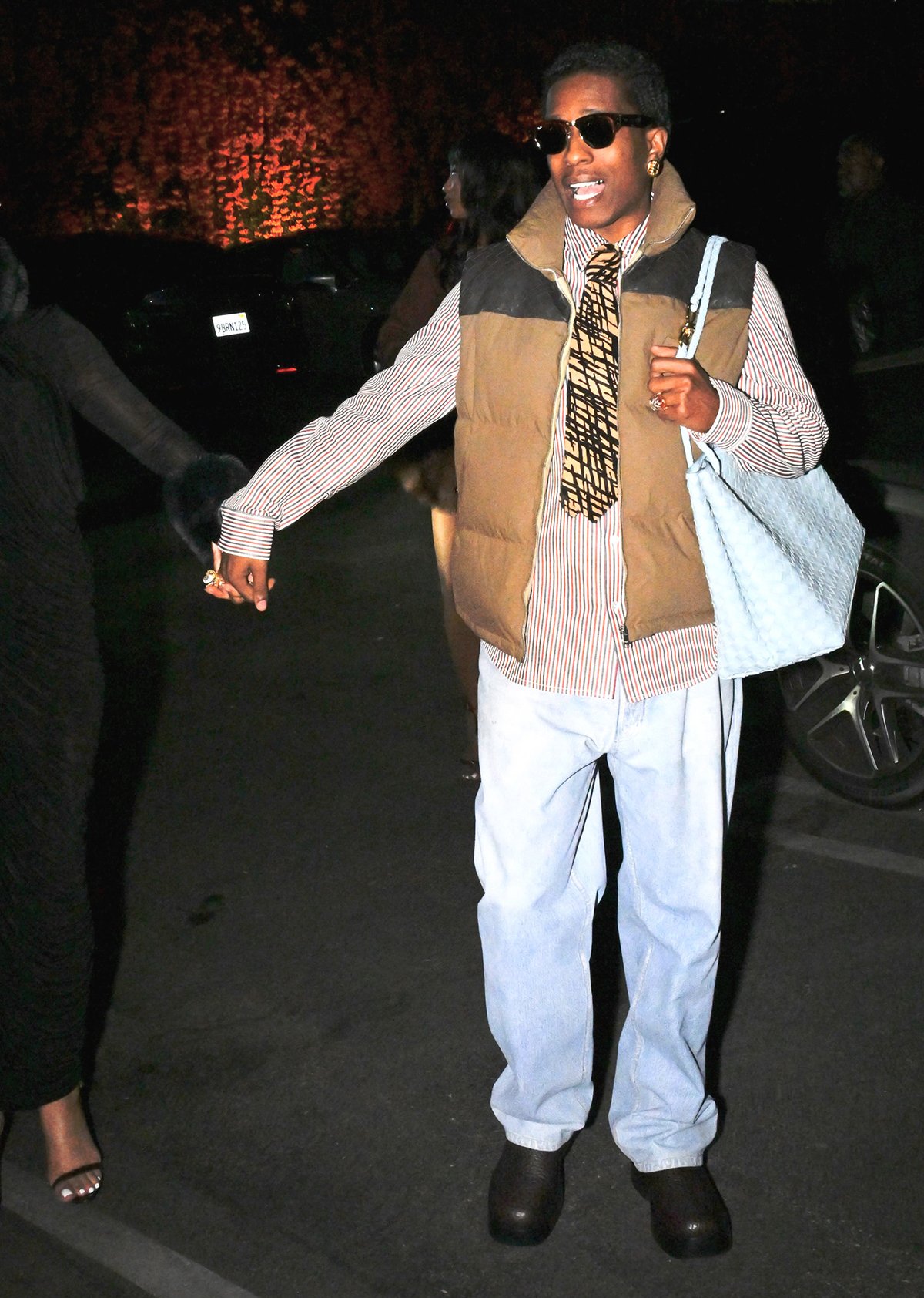 A$AP Rocky opts for his signature cool style, layering a pinstriped shirt underneath a khaki vest and styling it with a graphic yellow necktie and light-wash jeans