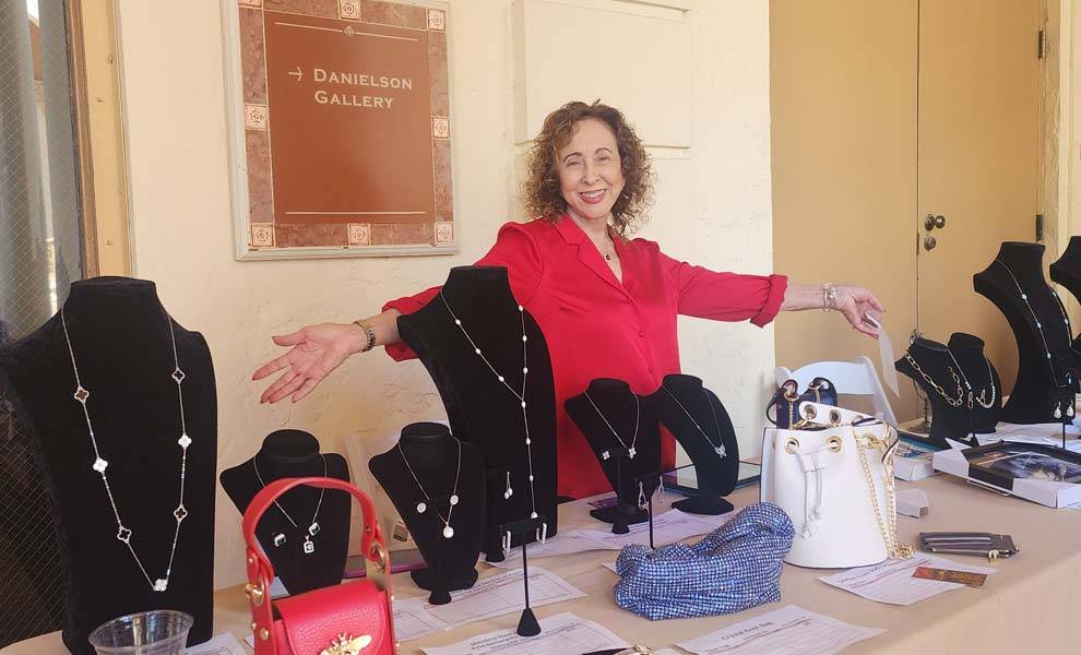 A woman stands beside a table filled with various bags and purses, showcasing a diverse collection of accessories.