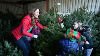 Catherine, Princess of Wales, helped by children, picks a Christmas tree during a visit to Peterley Manor Farm