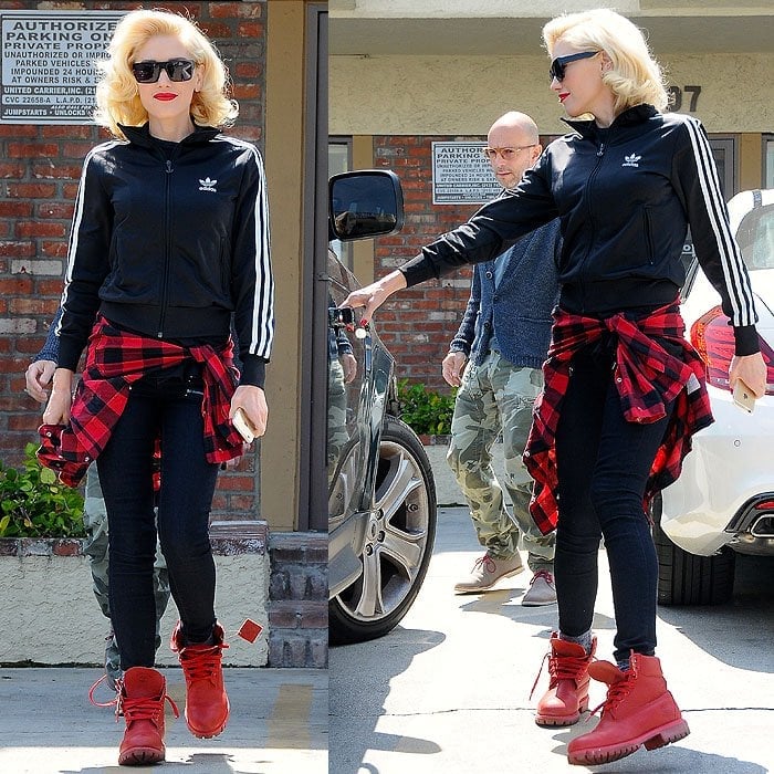 Gwen Stefani rocks bold red Timberland boots with a sporty Adidas track jacket, black skinny jeans, and a tied red plaid shirt for a cool, casual street style