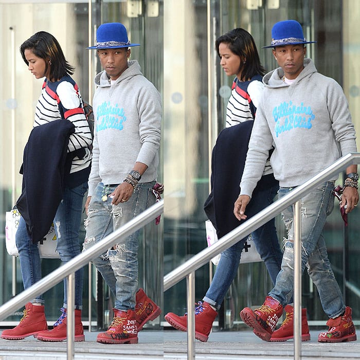 Pharrell Williams turns heads in custom red Timberland boots, ripped jeans, and a casual hoodie, while Helen Lasichanh complements him in a chic striped sweater