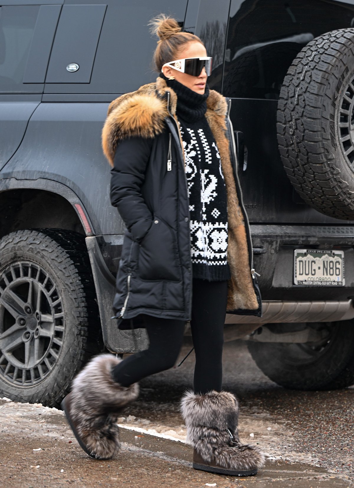 Jennifer Lopez strolling around Aspen in an apres-ski outfit featuring a sweater dress, a parka coat, and boots