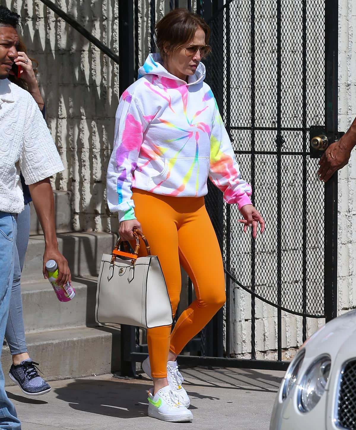 Jennifer Lopez stepped out in Los Angeles on June 2, 2022, wearing a Myrrhe rainbow tie-dye hoodie, Alo Yoga 7/8 high-waist airbrush leggings, Nike Air Force 1 sneakers, and carrying a white Gucci Diana bag with a TaylorMade Bling! Bodyarmor bling cup