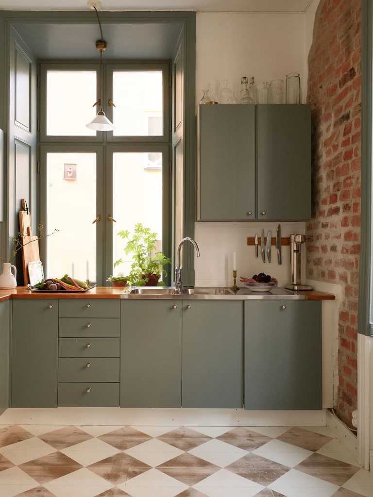 A green kitchen with a checkered floor and partly exposed brick wall