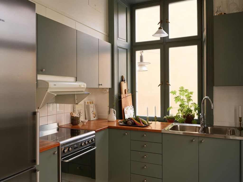 A green kitchen with a checkered floor and partly exposed brick wall