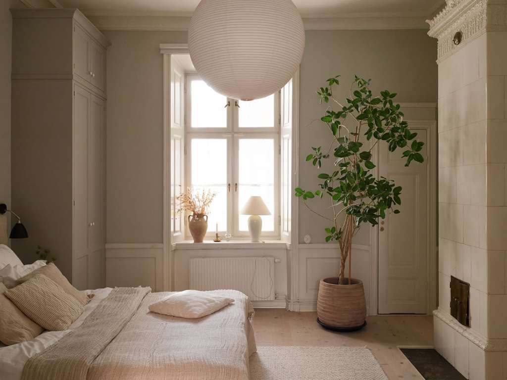 A bedroom with grey walls with green undertones, beige textiles and custom wardrobes flanking the bed