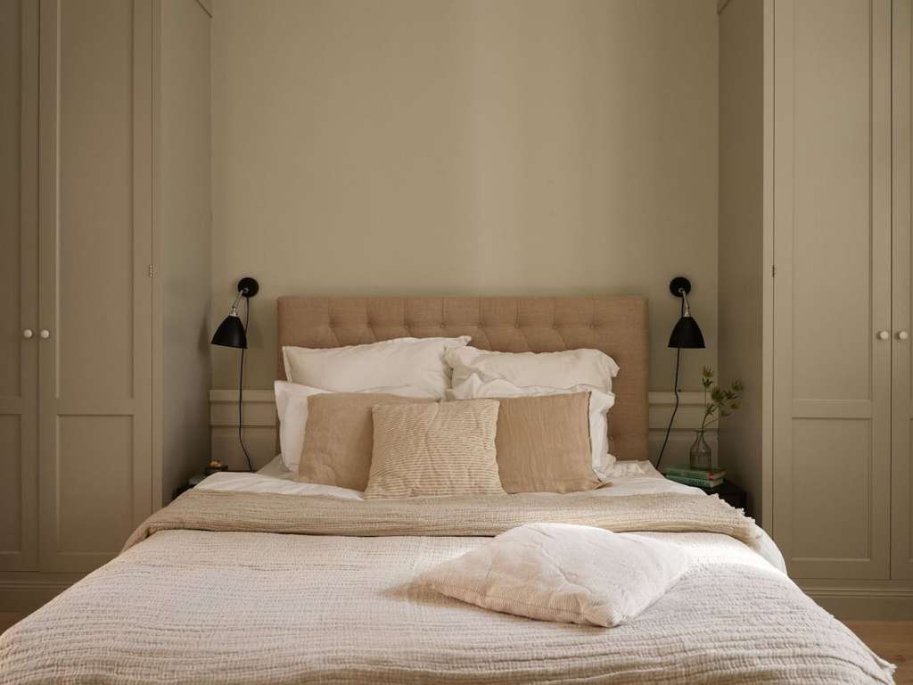 A bedroom with grey walls with green undertones, beige textiles and custom wardrobes flanking the bed