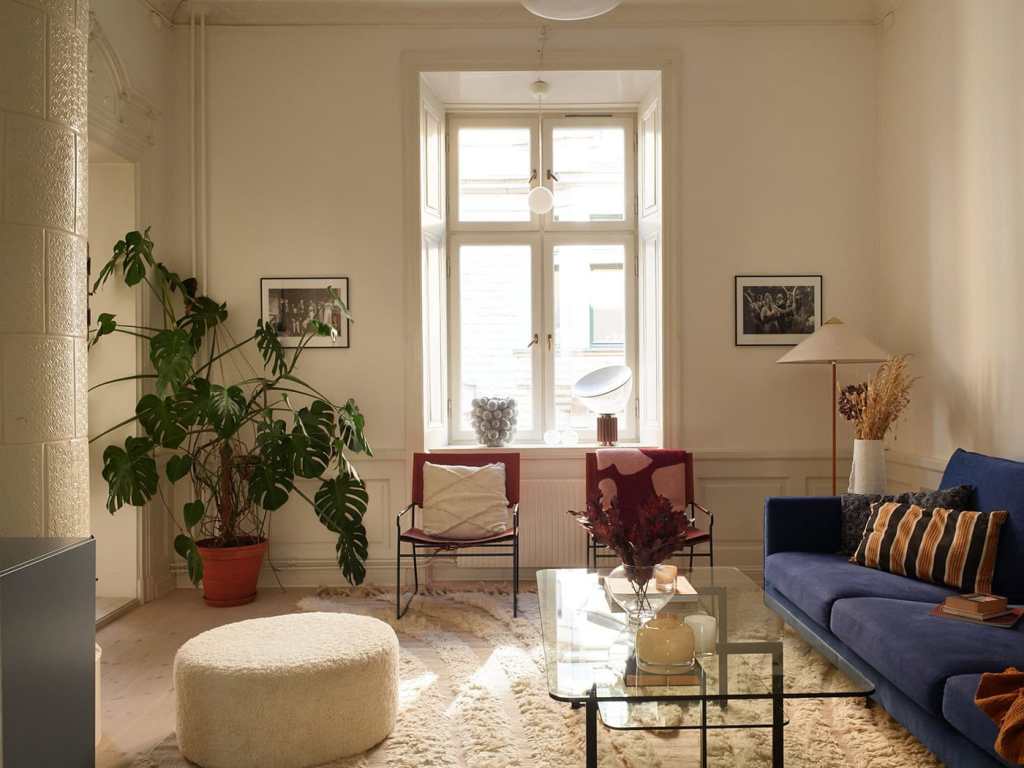 A white living room with a blue sofa and red armchairs