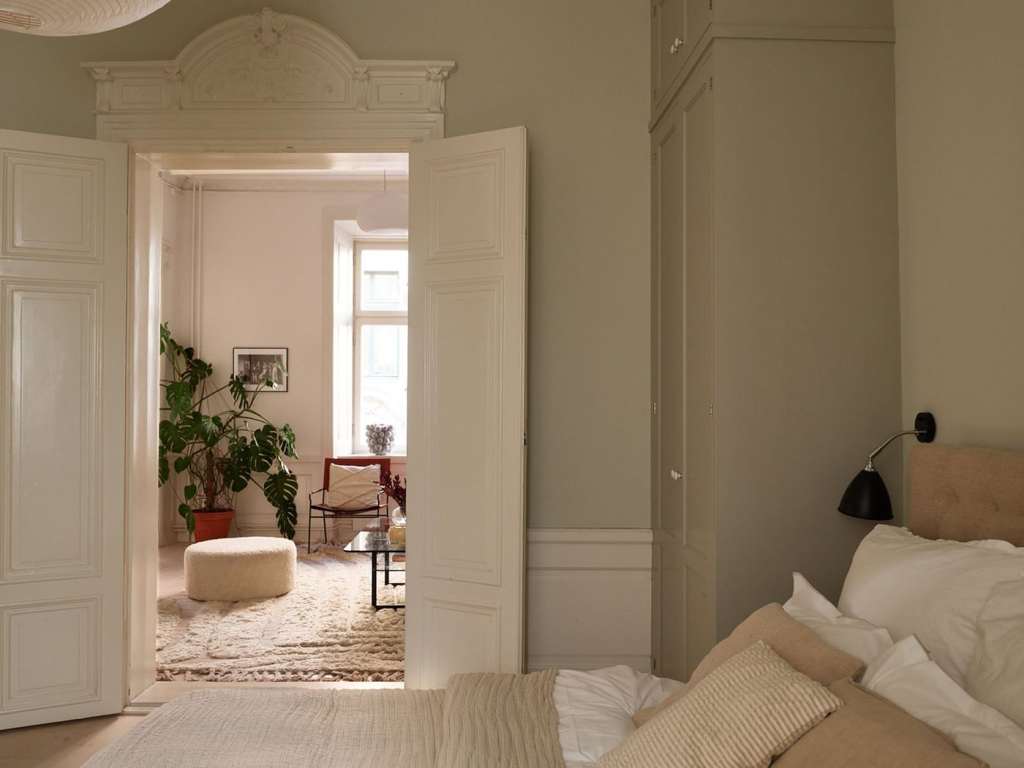 A bedroom with grey walls with green undertones, beige textiles and custom wardrobes flanking the bed