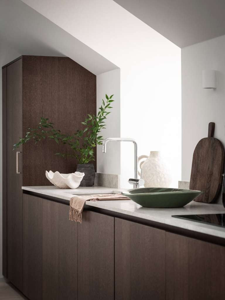 A dark oak kitchen with beige limestone countertops and chrome hardware