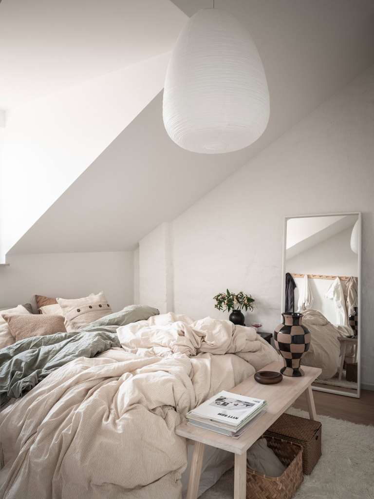 A bedroom with white walls and neutral, warm textiles