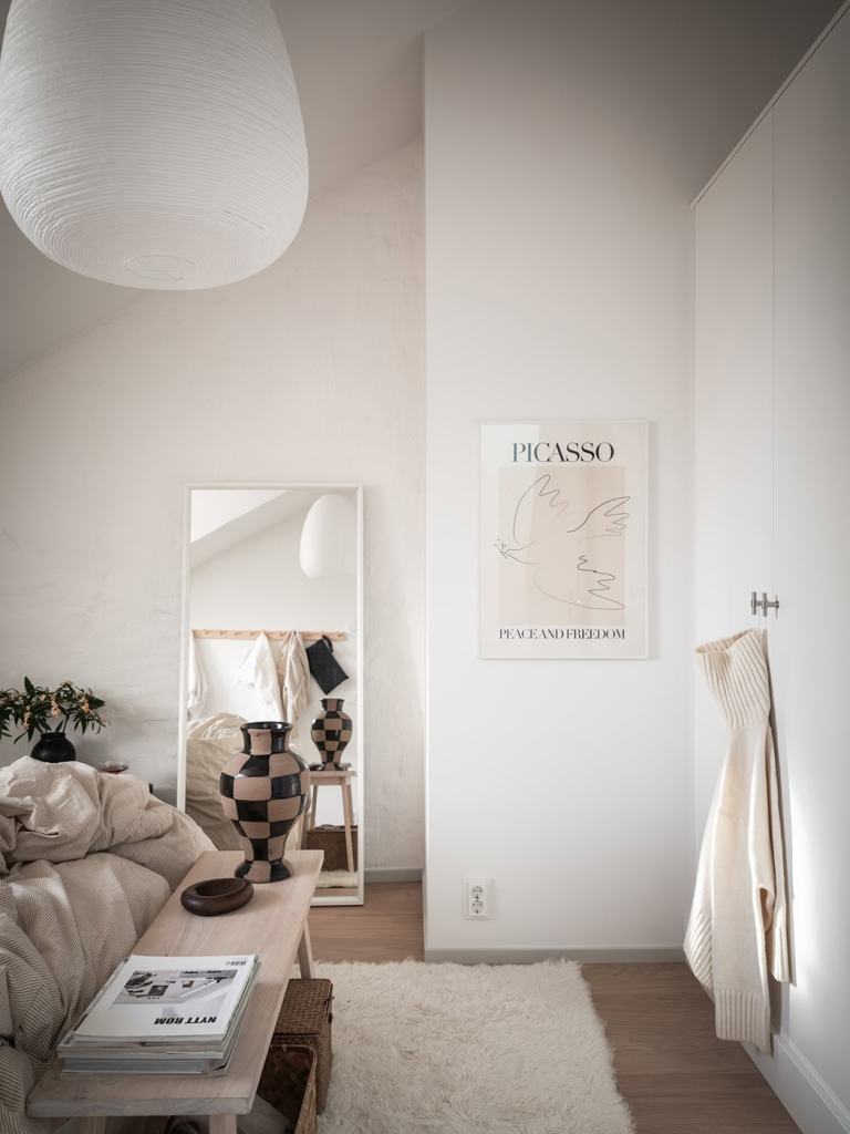 A bedroom with white walls and neutral, warm textiles