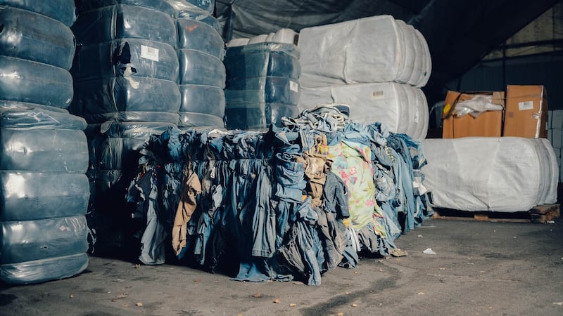 Bales of discarded clothes are stacked in a warehouse.