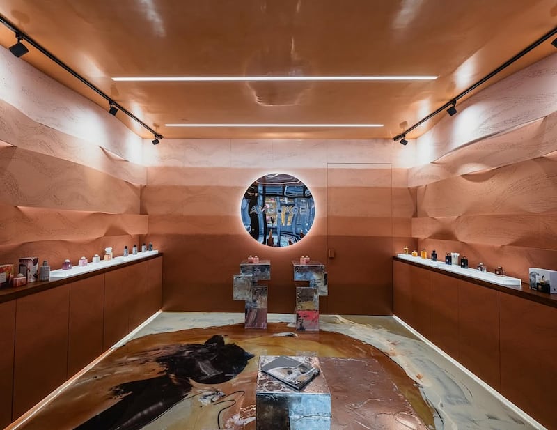 A small boutique in New York city is photographed from the inside. The two opposite walls feature counters where Amouage fragrances are displayed, and the walls seem like carved rock in a gradient of natural tones. The floor is a swirling, almost painterly-marble motif.