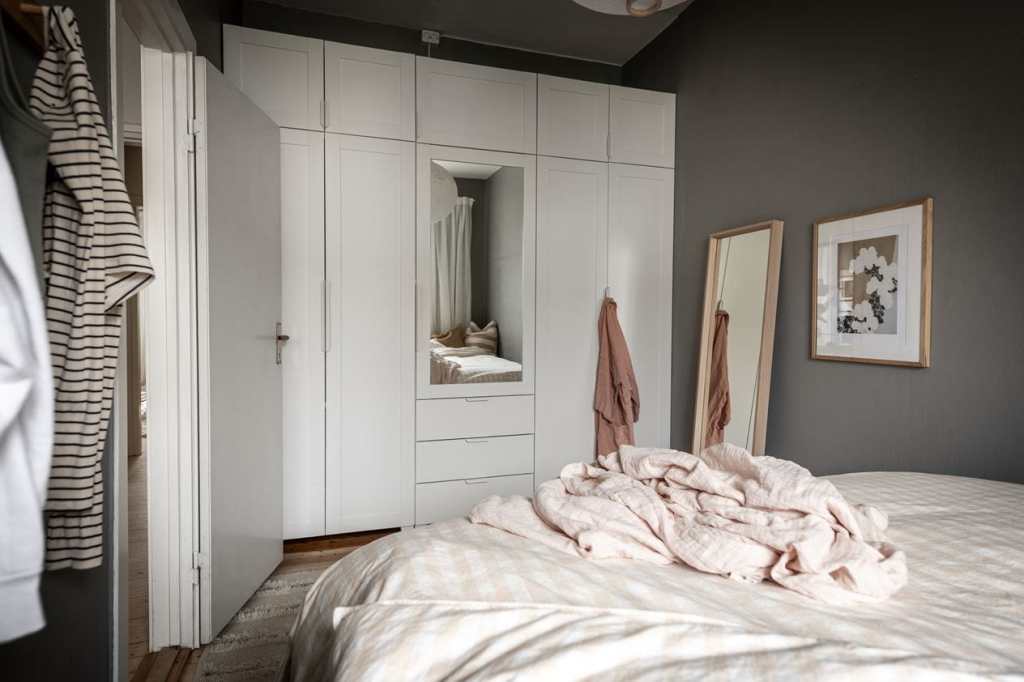 A white wall-to-wall wardrobe with a mirrored door in a dark grey bedroom