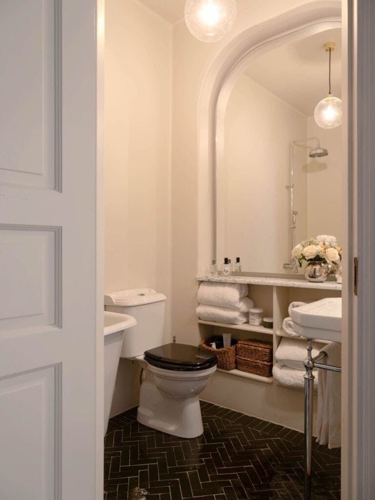 A black herringbone floor in a classic bathroom with an impressive mirror