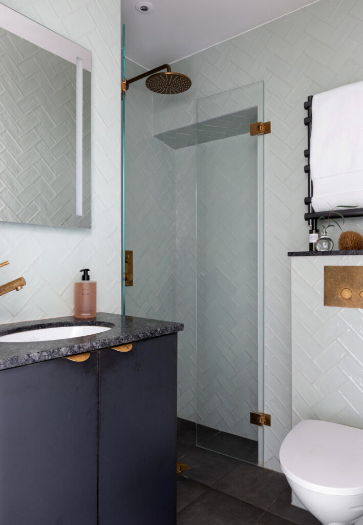 Light herringbone tile walls paired with dark stone flooring and burned gold hardware