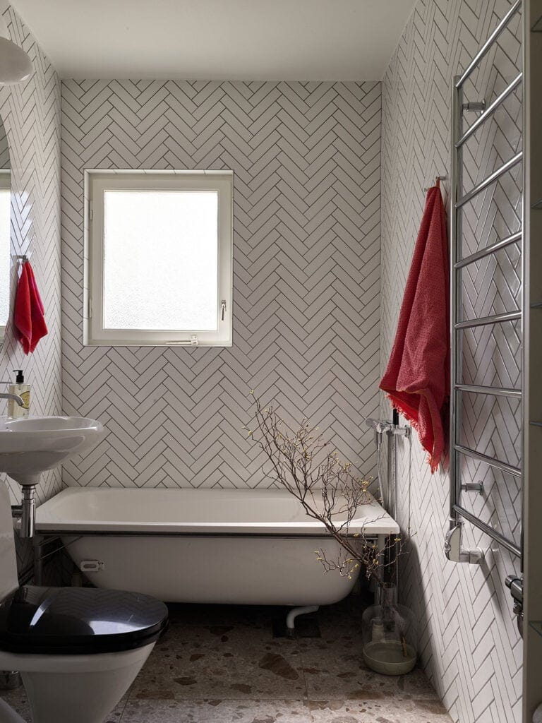 White herringbone tiles with dark grout covering the entirety of the walls in this bathroom