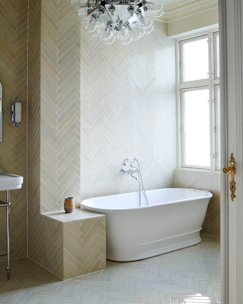 Beige elongated ceramic tiles in an impressive herringbone pattern in a historic bathroom with a soaking tub