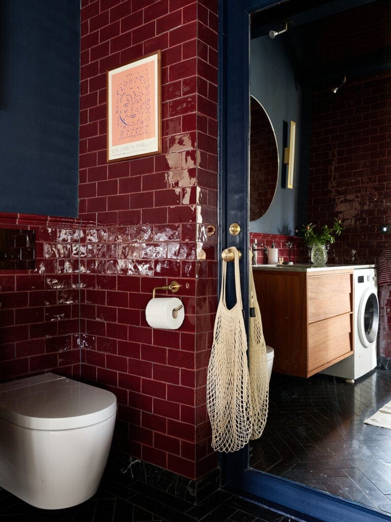 Dark-colored herringbone tiles paired with glossy burgundy wall tiles in a characterful bathroom